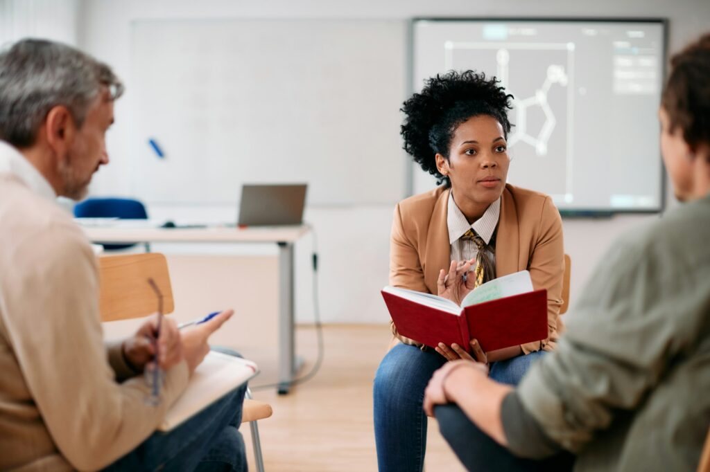 Black female professor having consultations with adult students at lecture hall.